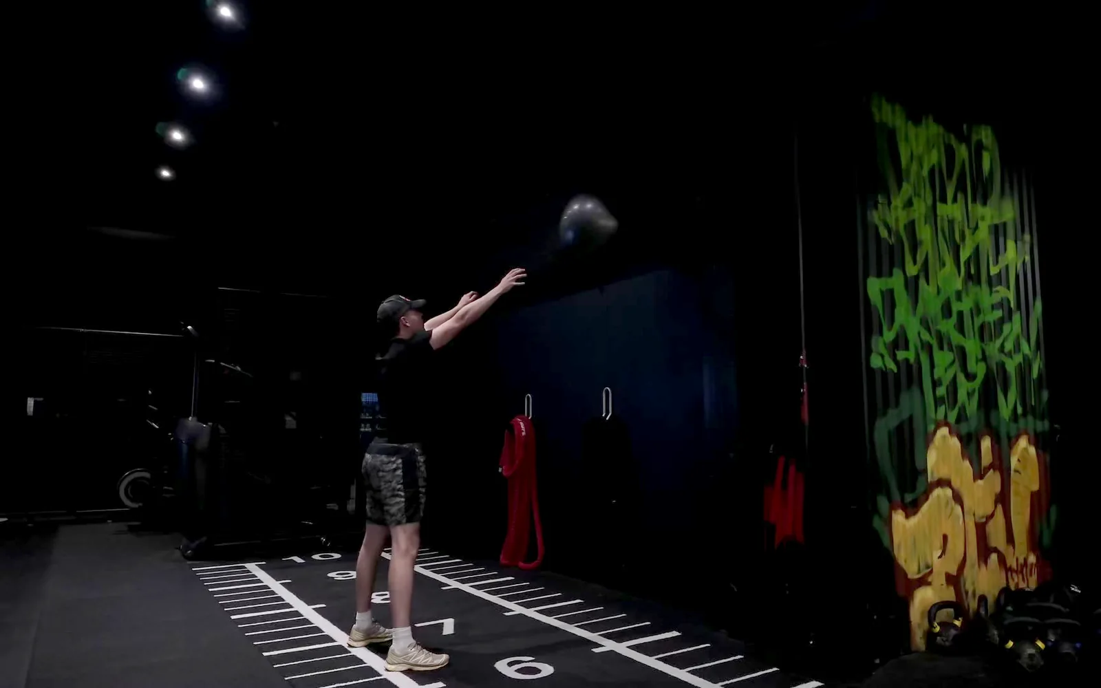 Mies heittää kuntopalloa ylös seinään wall ball -liikkeessä